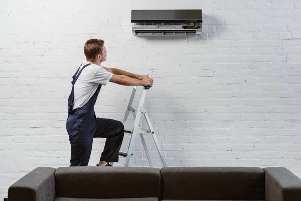 Professional air conditioner repairman standing on stepladder — Stock Photo