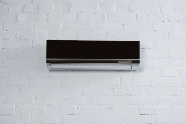 Moderno acondicionador de aire negro colgando en la pared de ladrillo blanco - foto de stock