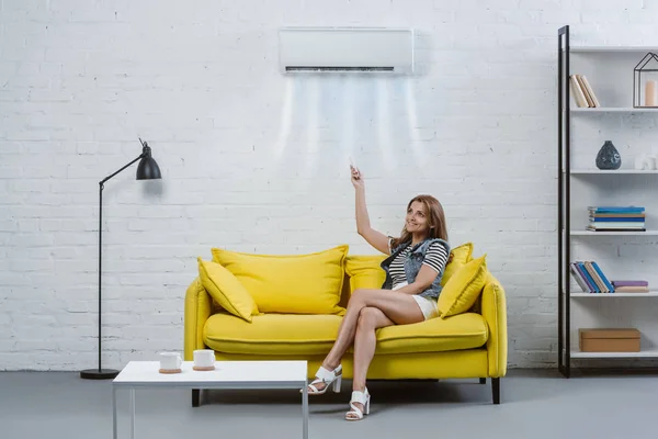 Attrayant jeune femme pointant vers climatiseur suspendu au mur avec télécommande — Photo de stock