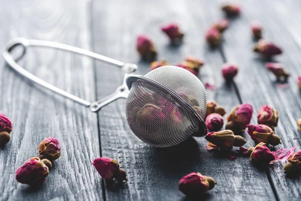 Dried rose buds tea and tea strainer on wooden table — Stock Photo