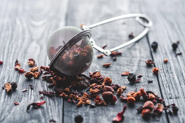 Savoureux thé noir aux fruits secs et passoire à thé sur table en bois — Photo de stock