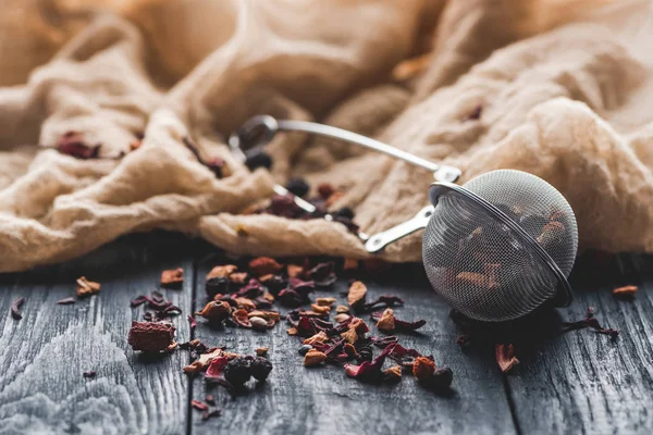 Tasty black tea with dried fruits, tea strainer and cloth on wooden table — Stock Photo