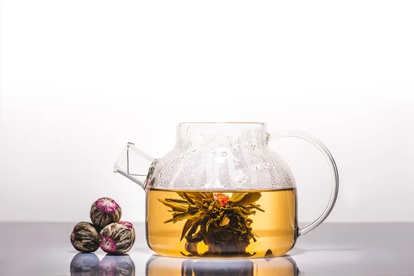 Théière en verre de thé chinois à fleurs avec boules de thé sur la table réfléchissante — Photo de stock