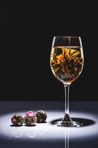 Glass of chinese flowering tea with tea balls on table isolated on black — Stock Photo