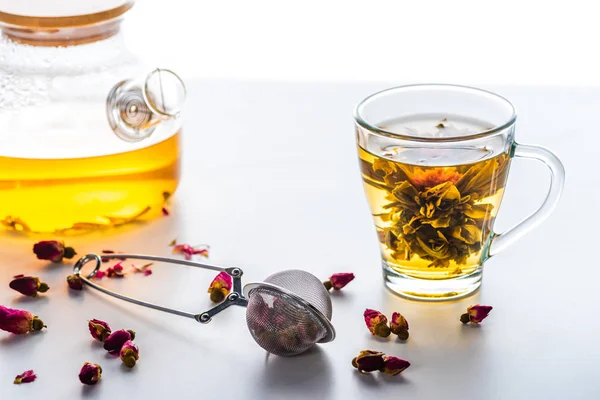 Cup of chinese flowering tea, teapot and tea strainer with dried rose buds — Stock Photo