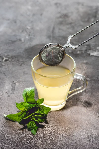 Healthy tea with mint and tea strainer on grey surface — Stock Photo