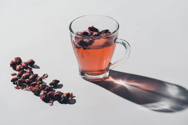 Красный чай из сушеных роз в чашке на белом столе — стоковое фото