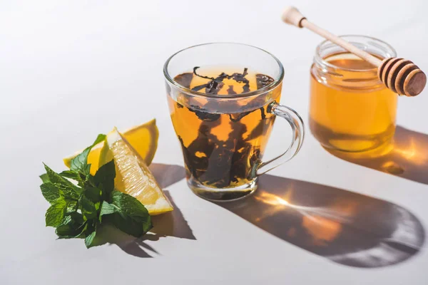 Здоровий чорний чай з медом, лимоном і м'ятою в чашці на білому столі — стокове фото