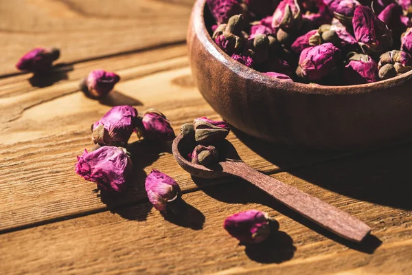 Dried rose buds in wooden bowl and spoon on wooden table — Stock Photo