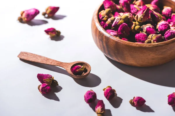 Dried rose buds in wooden bowl and spoon on white tabletop — Stock Photo