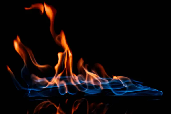 Vue rapprochée de la flamme orange et bleue brûlante sur fond noir — Photo de stock