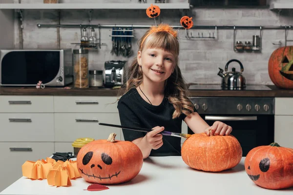 Porträt des süßen lächelnden Kindes, das zu Hause in der Küche Kürbisse für Halloween bemalt — Stockfoto