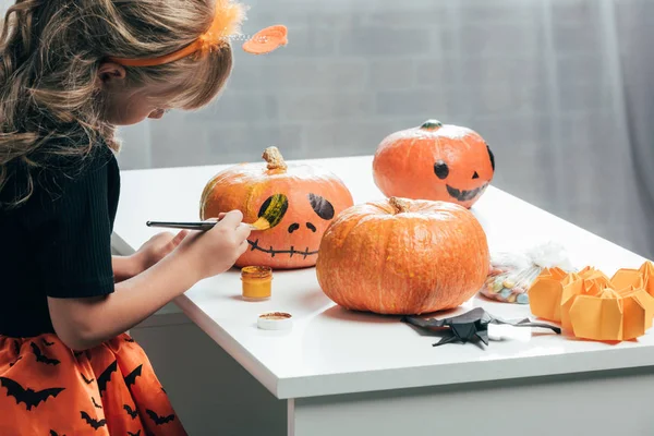 Vista lateral de lindo niño pintando calabazas para Halloween en casa - foto de stock