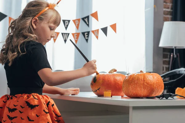 Seitenansicht fokussiertes Kind bemalt Kürbisse für Halloween zu Hause — Stockfoto