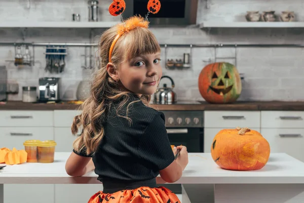 Rückansicht eines Kindes im Halloween-Kostüm an der Tischplatte mit Kürbissen in der heimischen Küche — Stockfoto