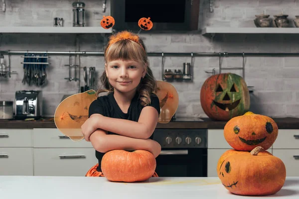 Kleines Kind im Halloween-Kostüm steht mit Kürbissen in der heimischen Küche an der Tischplatte — Stockfoto