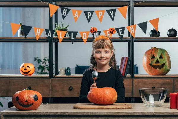Portrait of smiling kid at tabletop with pumpkins and hanging happy halloween flags behind at home — Stock Photo