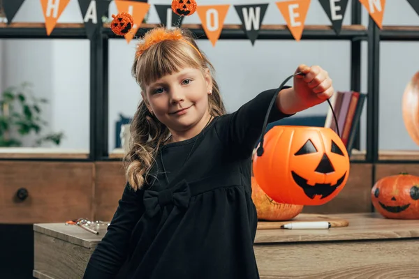 Portrait of little kid showing pumpkin bucket for sweets at home — Stock Photo