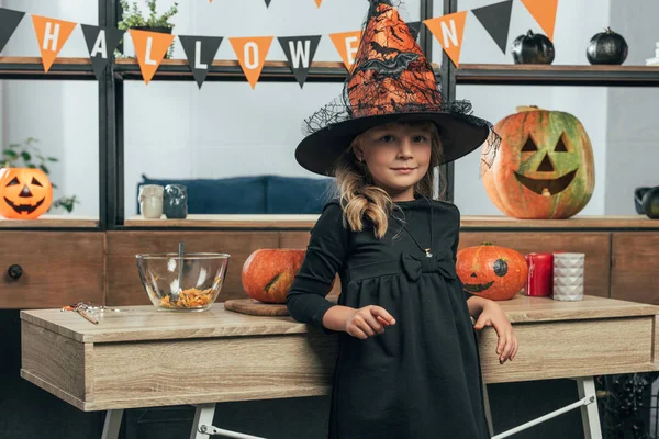 Portrait of adorable kid in witch halloween costume leaning on wooden tabletop at home — Stock Photo