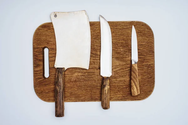 Top view of different kitchen knives on wooden chopping board isolated on grey — Stock Photo