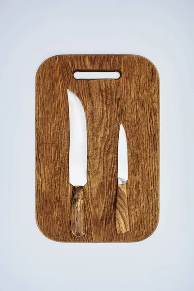 Вид зверху на два кухонні ножі на дерев'яній обробній дошці ізольовані на сірому — стокове фото