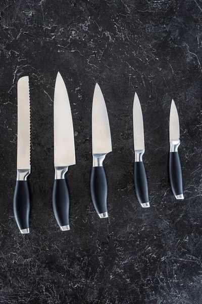 Top view of various kitchen knives arranged on black marble surface — Stock Photo