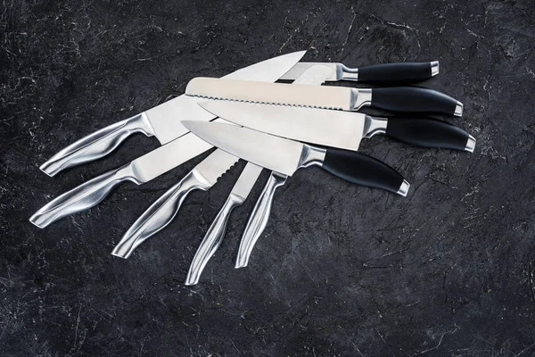 Set of various kitchen knives arranged on black, top view — Stock Photo