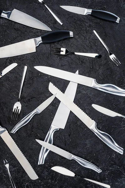 Vista superior de várias facas de cozinha e garfos dispostos na superfície preta — Fotografia de Stock