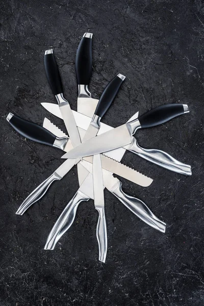 Top view of various kitchen knives arranged on black surface — Stock Photo