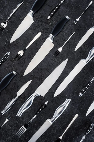 Top view of various forks and knives on black surface — Stock Photo