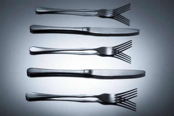 Shiny stainless steel forks and knives reflected on grey — Stock Photo