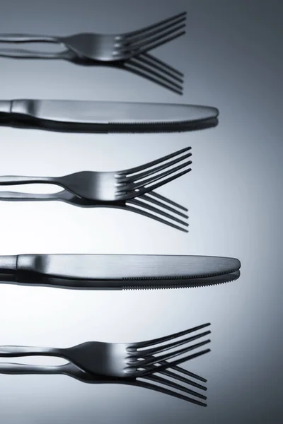 Крупним планом блискучі виделки і ножі, відображені на сірому — стокове фото