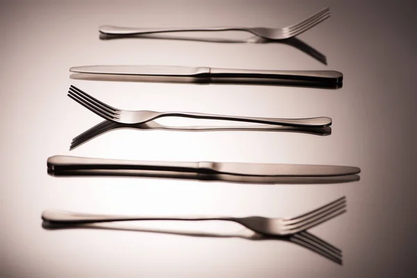 Close-up view of shiny forks and knives arranged on grey — Stock Photo