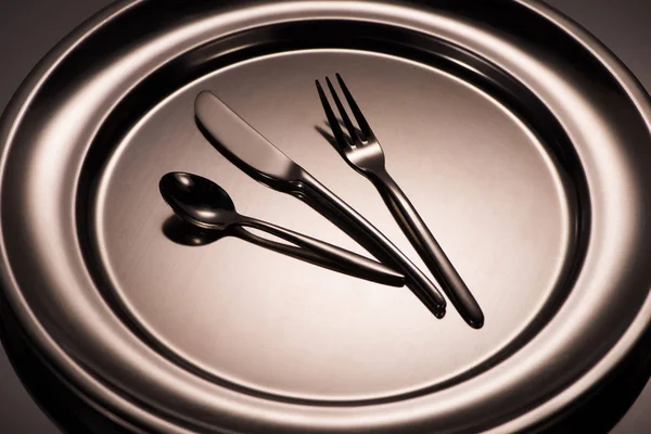 Close-up view of spoon, fork and knife on shiny plate on grey — Stock Photo