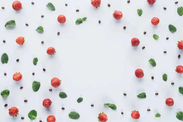 Vista superior de marco redondo hecho de fresas maduras con hojas de menta y granos de café en la superficie blanca - foto de stock