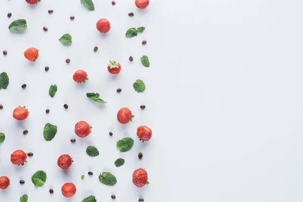 Vue de dessus des fraises mûres avec des feuilles de menthe et des grains de café sur la surface blanche — Photo de stock