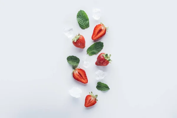 Vue de dessus des fraises mûres coupées en deux avec des feuilles de menthe et des glaçons sur la surface blanche — Photo de stock