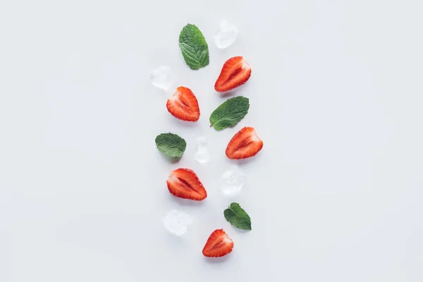 Vista superior de fresas a la mitad con hojas de menta y cubitos de hielo en la superficie blanca - foto de stock