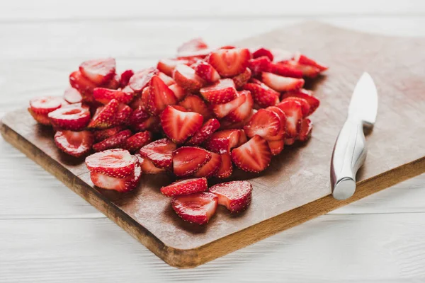 Tabla de cortar de madera con fresas en rodajas y cuchillo en la mesa blanca - foto de stock