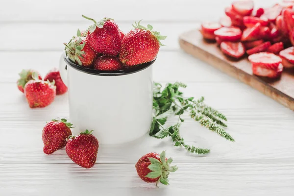 Reife Erdbeeren im Becher auf weißer Holzoberfläche mit Schneidebrett — Stockfoto