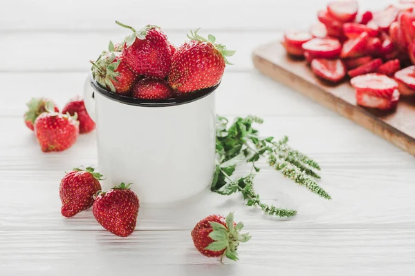 Fresas maduras en taza sobre superficie de madera blanca con tabla de cortar - foto de stock