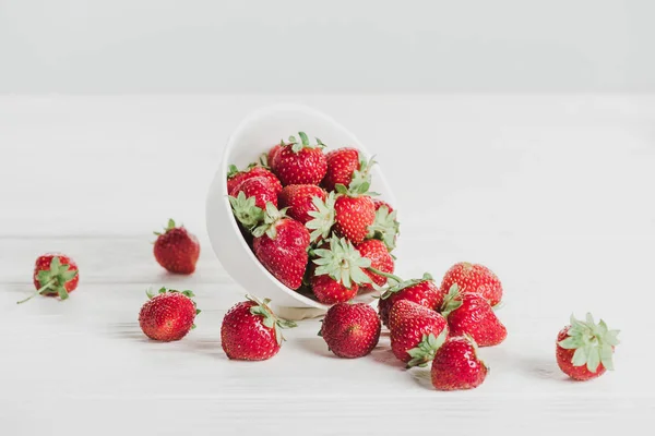 Gros plan des fraises renversées du bol sur la surface blanche — Photo de stock