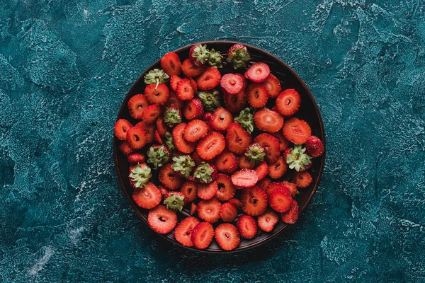 Top view of bowl with ripe sliced strawberries on blue concrete surface — Stock Photo