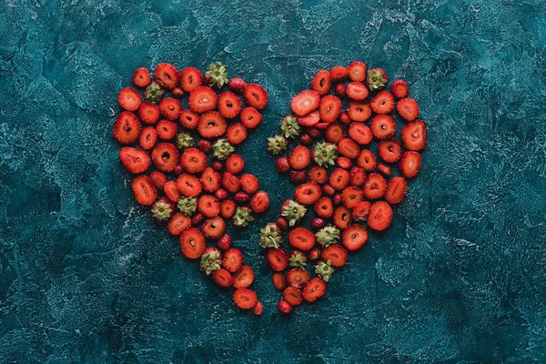 Draufsicht auf halbiertes Herzschild aus reifen Erdbeeren auf blauer Betonoberfläche — Stockfoto