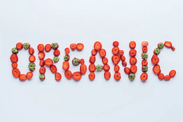 Vue du dessus de l'inscription biologique faite de fraises tranchées sur une surface blanche — Photo de stock