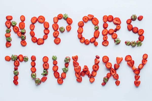 Top view of part of alphabet letters made of fresh sliced strawberries on white surface — Stock Photo