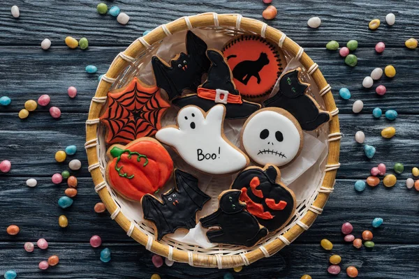 Top view of wicker basket with homemade spooky halloween cookies surrounded by candies on wooden table — Stock Photo