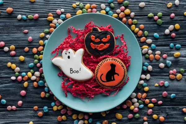 Elevated view of plate with halloween cookies surrounded by colorful candies on wooden table — Stock Photo