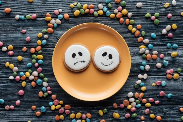 Top view of plate with halloween cookies surrounded by colorful candies on wooden table — Stock Photo