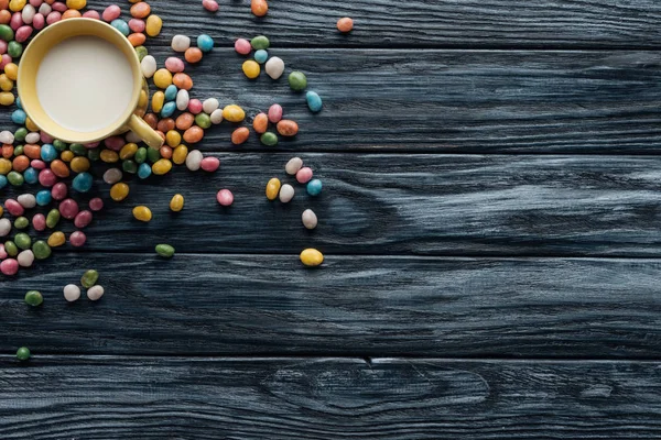 Vue surélevée de bonbons colorés et tasse avec du lait sur fond en bois — Photo de stock